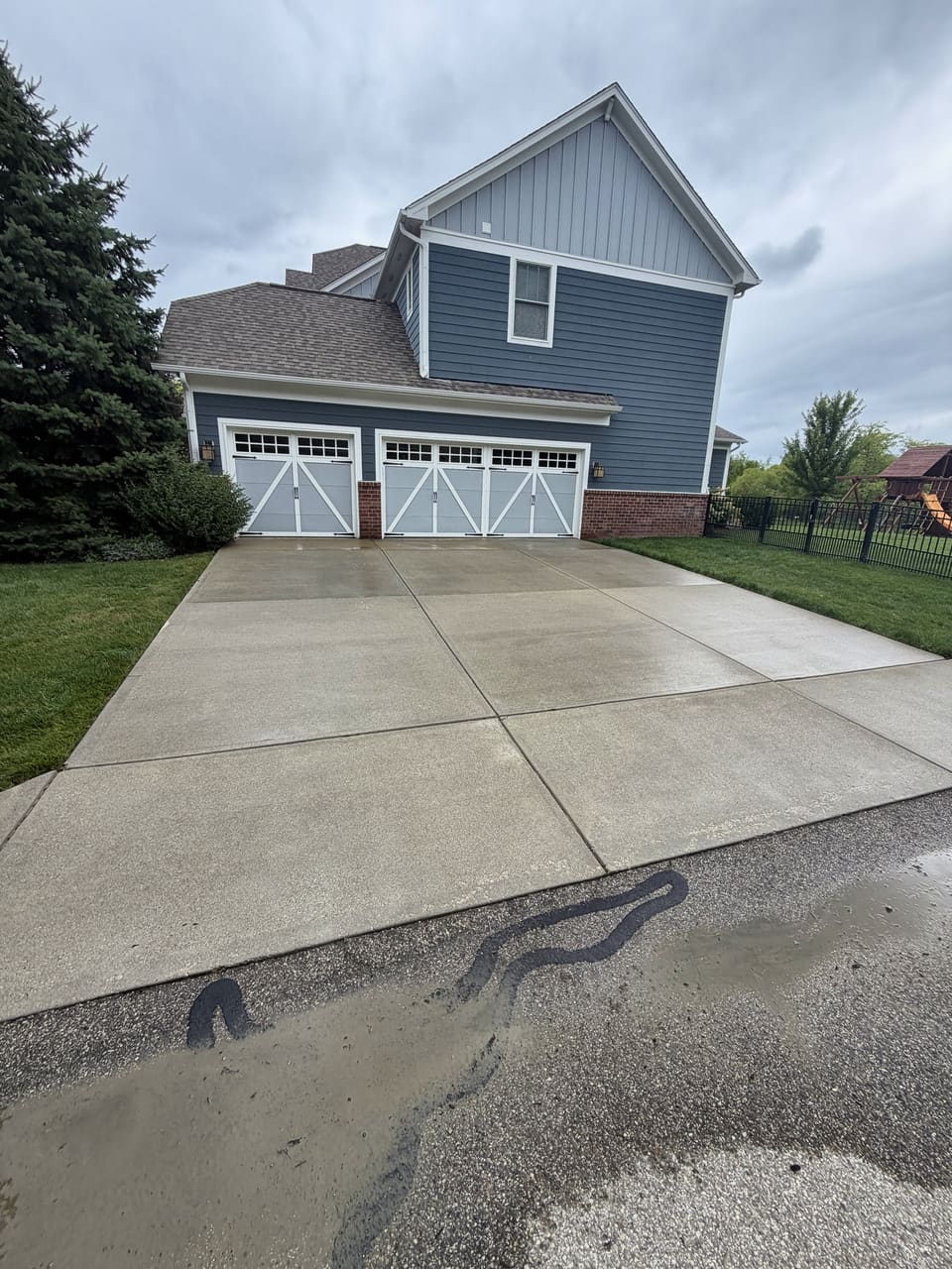 Clean driveway leading to a blue two story home with carriage garage doors