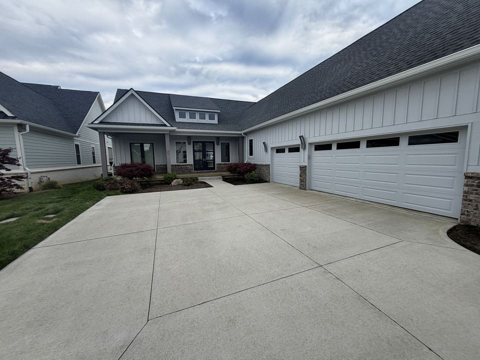 Wide clean concrete driveway in front of a white farmhouse with a three car garage