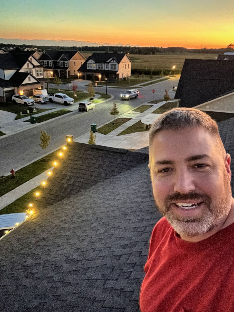 A Trojan crew member on a roof at sunset with a lit roofline behind him