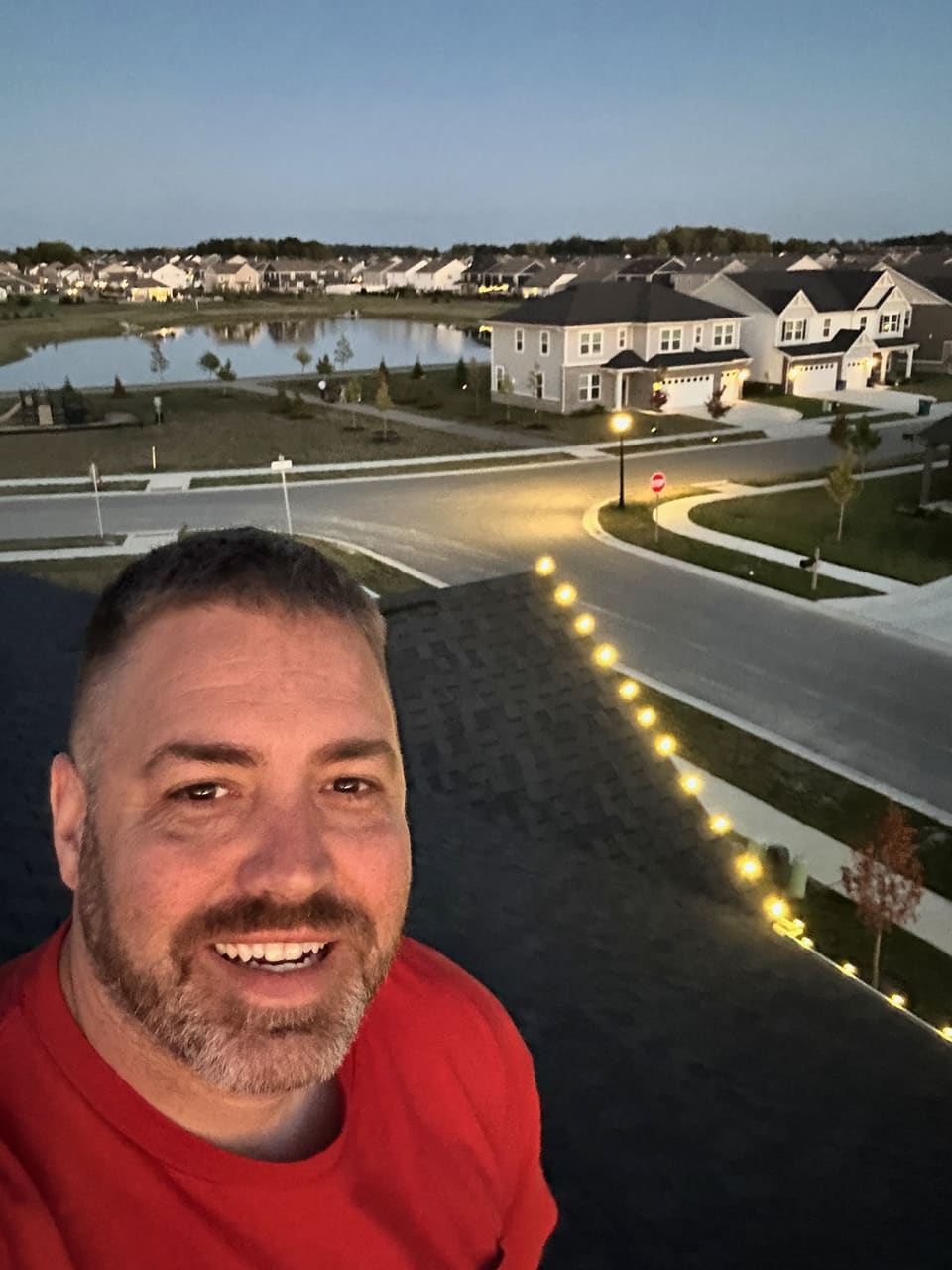 A Trojan crew member on a rooftop at dusk next to a roofline of warm white lights