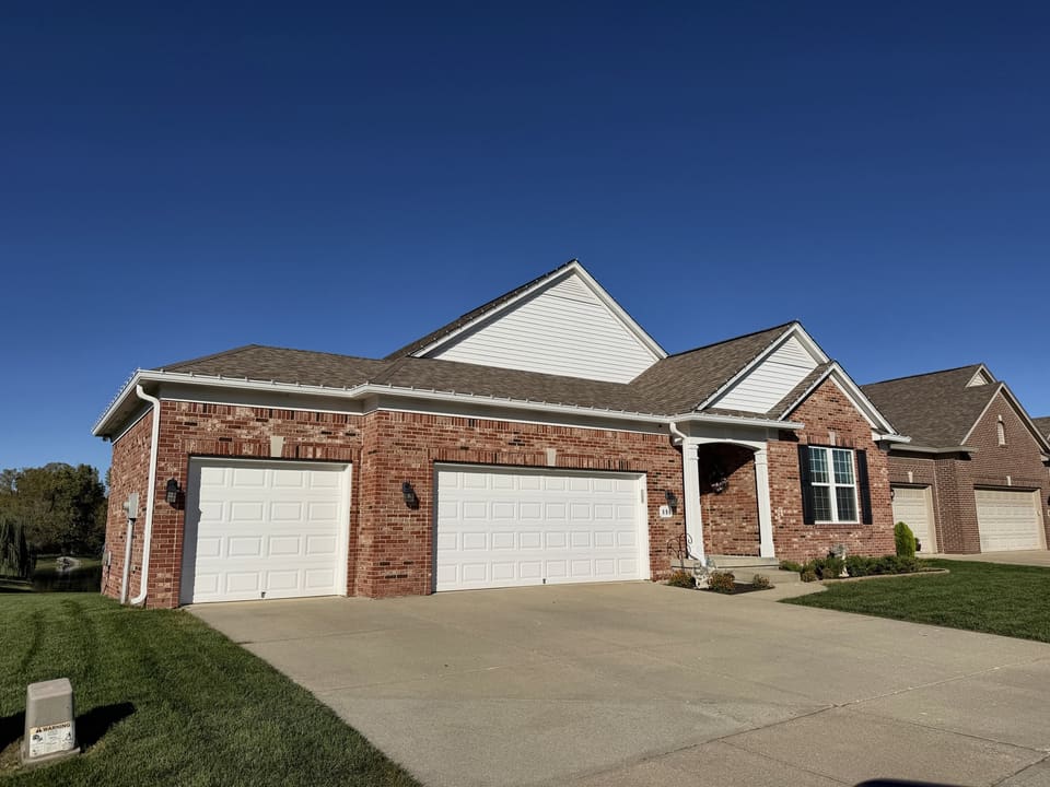 Brick ranch home with two white garage doors and a clean driveway on a clear afternoon