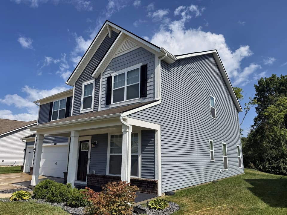 Freshly washed two story home with black shutters under a bright sky