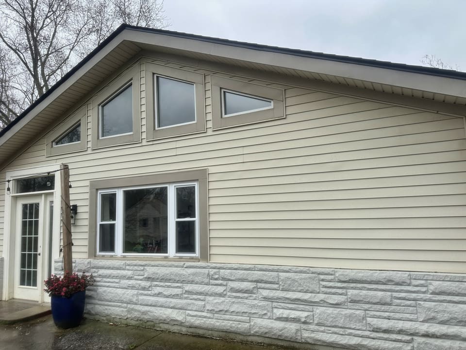 Back of a ranch home with cream siding and stone skirting after washing