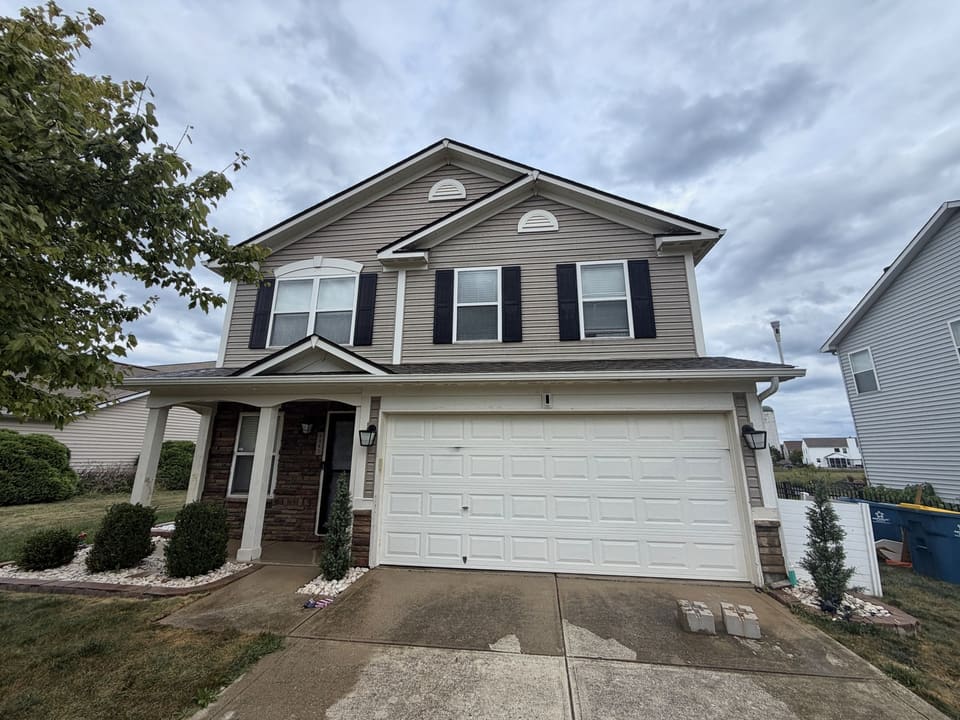 Tan two story home with a white garage door after a house wash