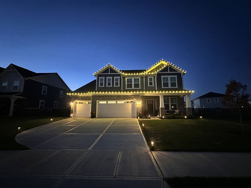 Two story home with warm white roofline lights at blue hour