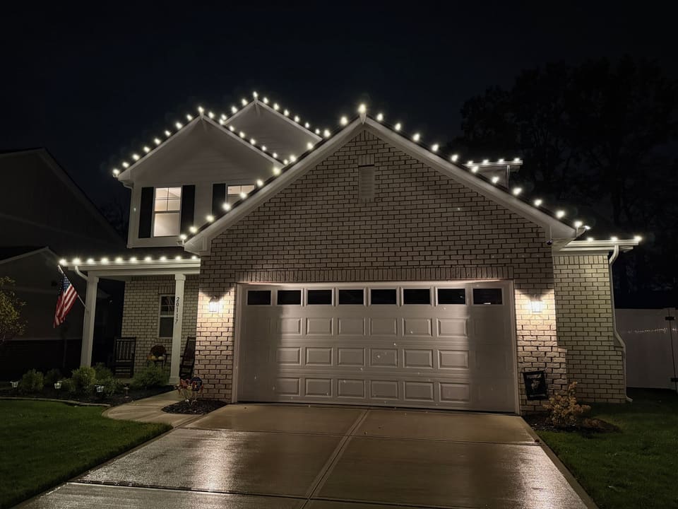 Brick home with a white roofline of lights over a lit garage