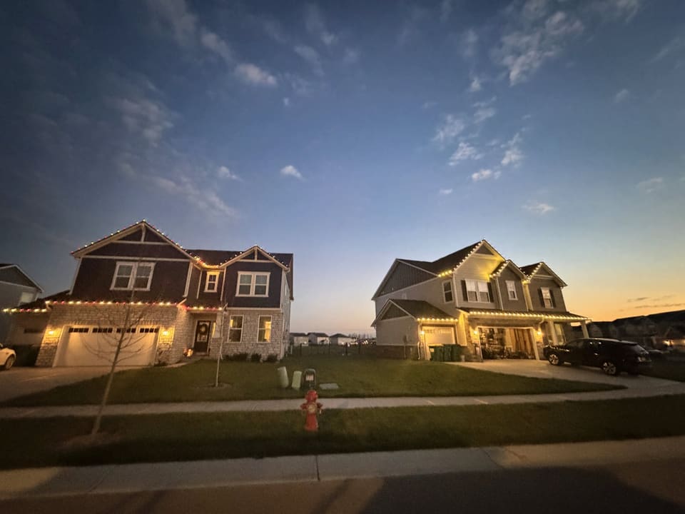 Two neighboring homes with warm roofline lights at dusk