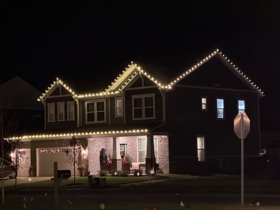 Dark two story home with white lights tracing three gables