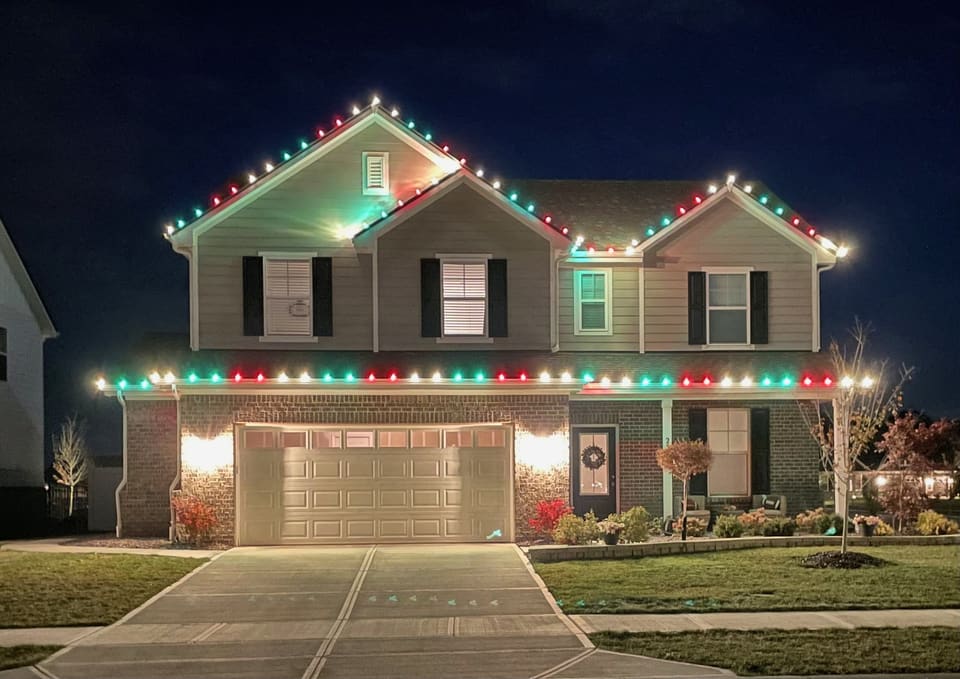 Two story home lit with alternating red, green, and white bulbs along every roofline