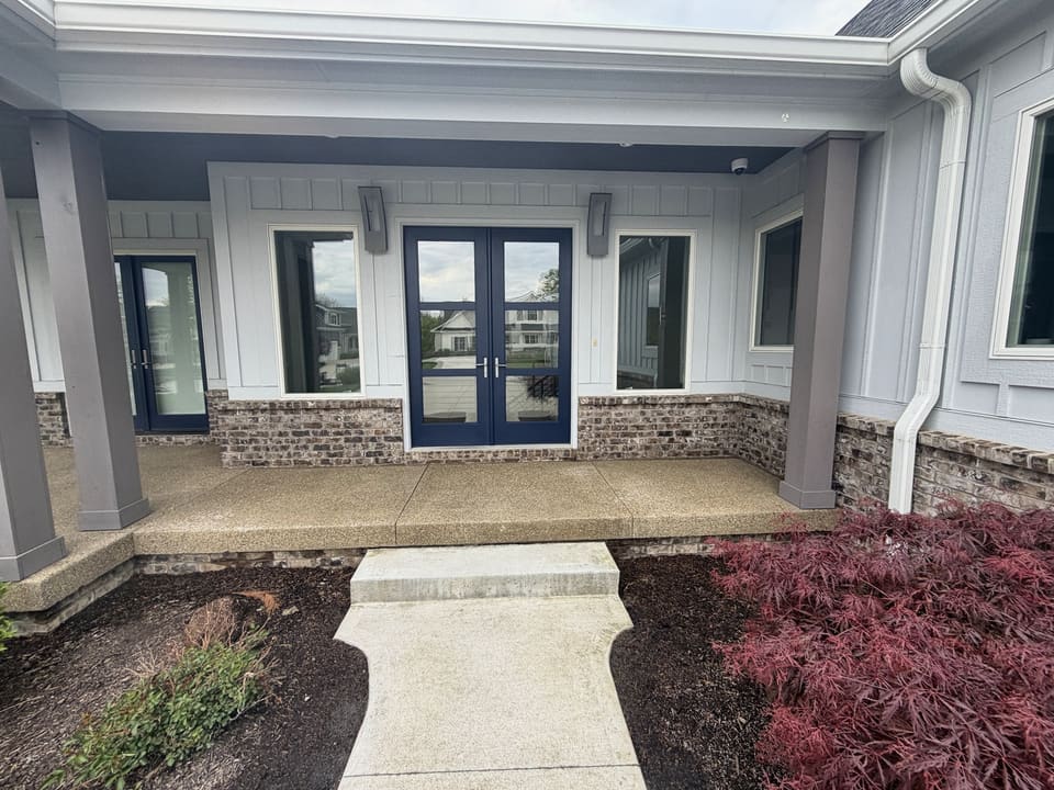 Covered front porch with clean concrete and blue double doors