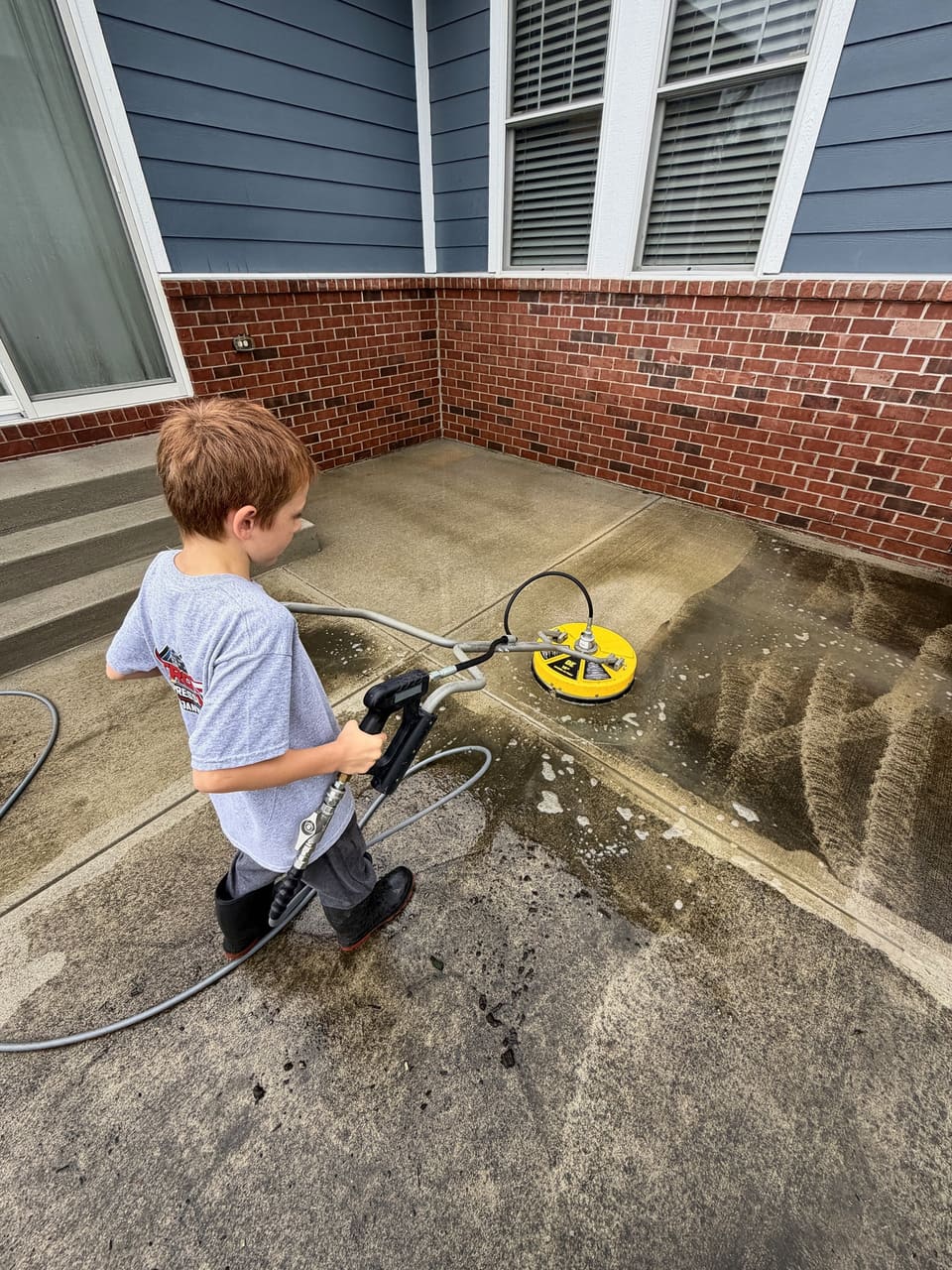 A young helper guiding a surface cleaner across a brick edged patio