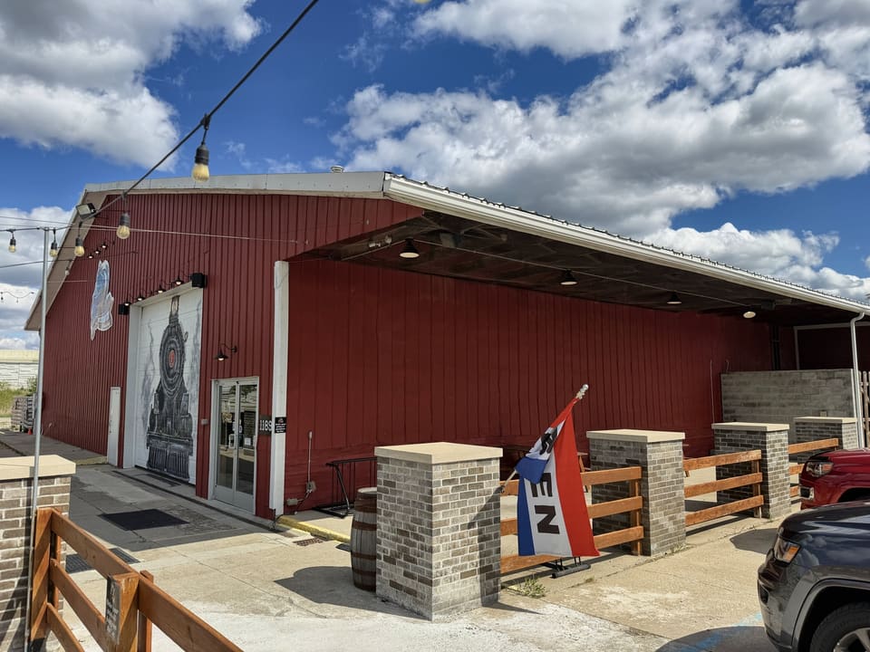 Front of a red barn venue with brick pillars and wood fencing after washing