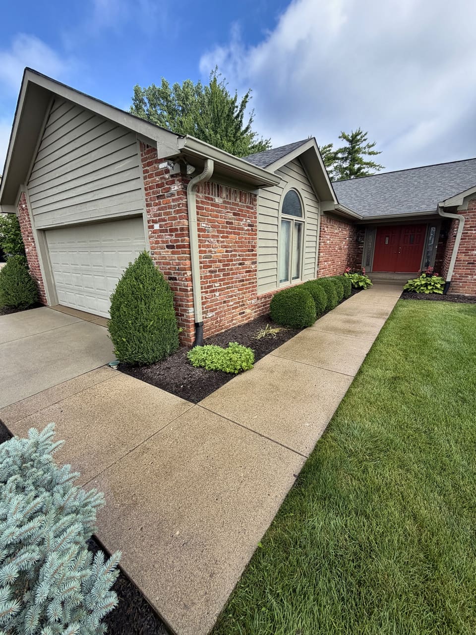 Clean walkway along a brick ranch home with trimmed shrubs