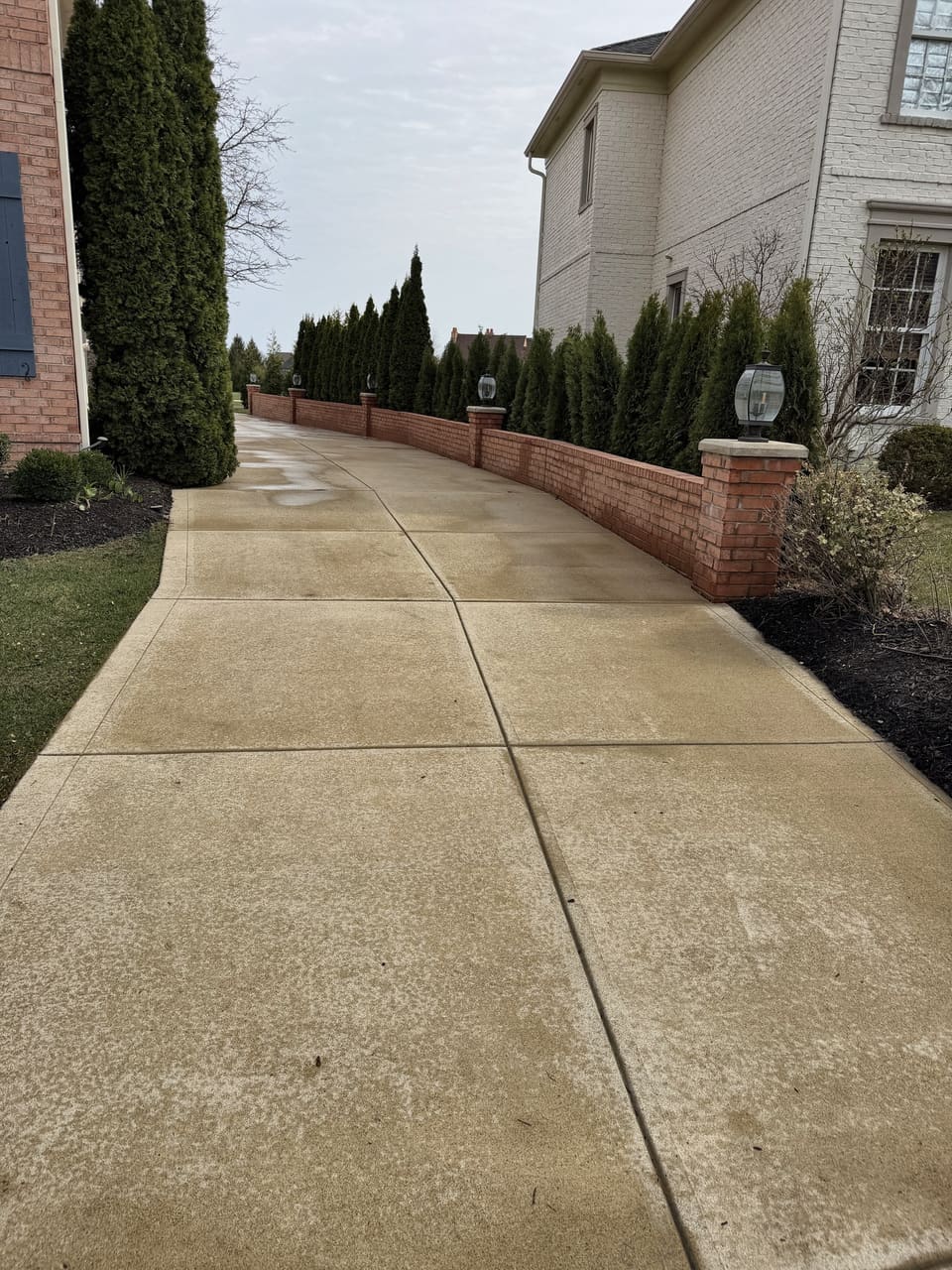 Concrete walk along a low brick wall beside a large home