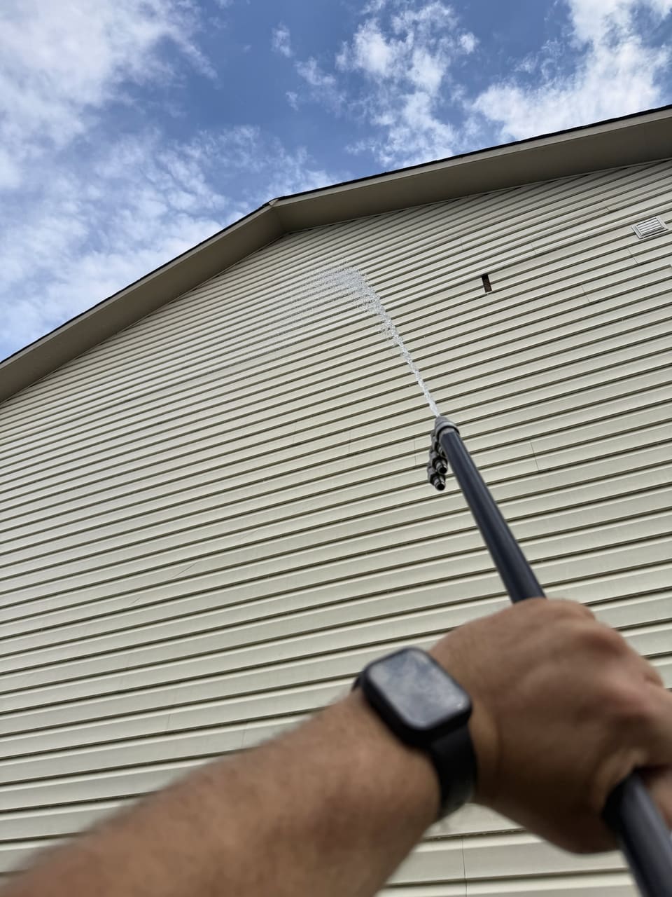 Soft wash spray rinsing a vinyl siding wall up to the roofline